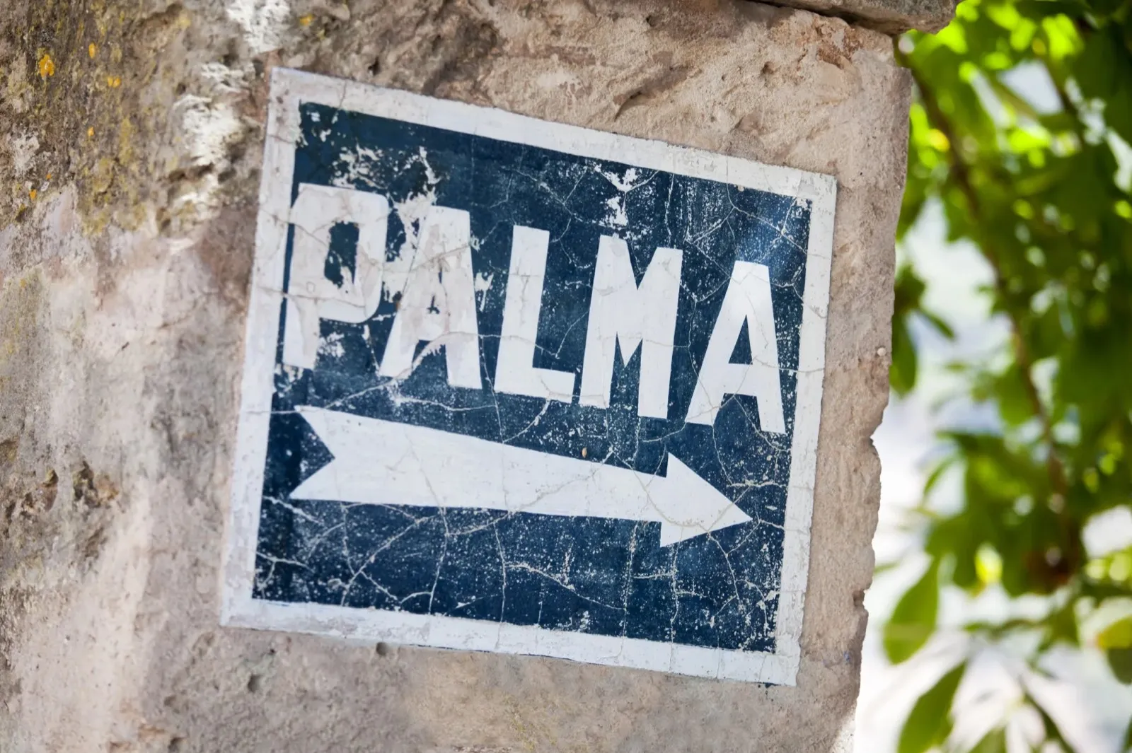 An old painted road sign on a stone wall, pointing to Palma